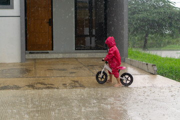 Obraz premium Daughter riding bike on rainy day with red coat