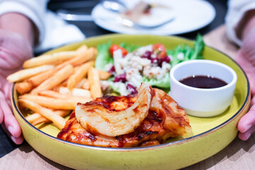 Delicious grilled chicken steak topped with pineapple, served with crispy fries, fresh salad, and a side of BBQ sauce on a yellow plate.
