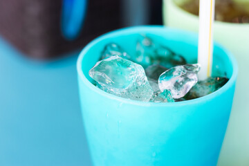 Ice cubes in a bright blue plastic cup with a straw, capturing a refreshing moment on a hot day. Minimal background and vibrant colors create a summery feel.