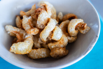 Close-up of crispy pork rinds in a white bowl, a savory and crunchy snack made from fried pork skin, popular in various cuisines around the world.