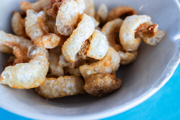 Close-up of crispy pork rinds in a white bowl, a savory and crunchy snack made from fried pork skin, popular in various cuisines around the world.