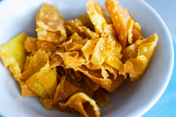 Crispy fried wonton wrappers in a white bowl. Golden, crunchy texture perfect as a snack or topping, showcasing delicious Asian-style street food simplicity.