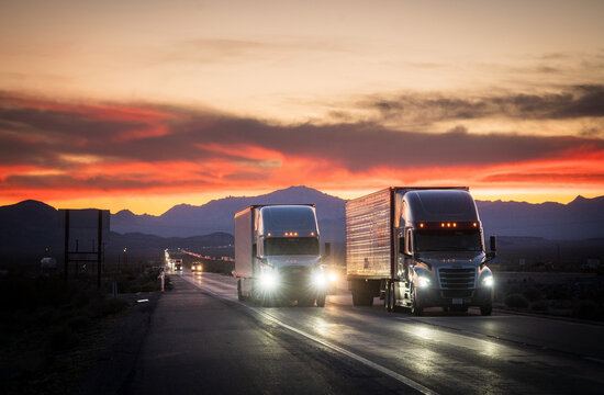 Transport semi trucks travel along Interstate Five, I-5, near near Stockton California, USA, at sunset.