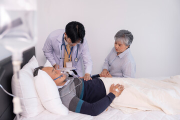 Fototapeta premium scene of a sad elderly woman holding hands a dying man on bed,on IV drip and oxygen,a doctor is physically examine,concept palliative care,end of life care