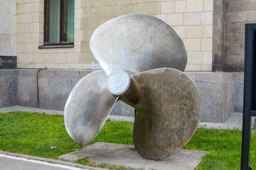 Large Modern Metal Propeller Sculpture in Urban Park Setting with Building Background