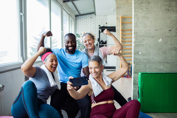 Diverse group of happy seniors and fitness trainer taking a post-workout selfie at the gym