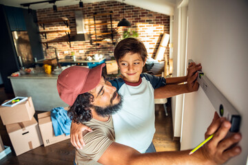 Young father and son measuring a wall in their new home after moving in