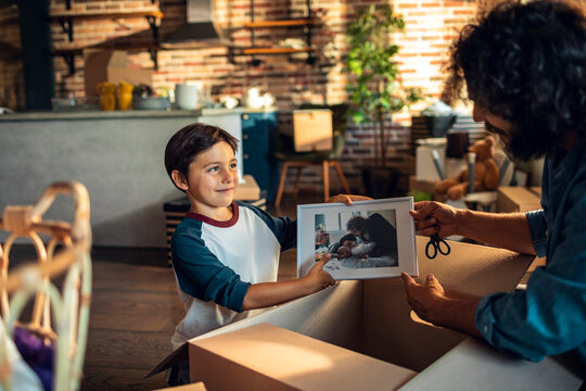 Young father and son holding a family picture while unpacking boxes after moving in their new home apartment