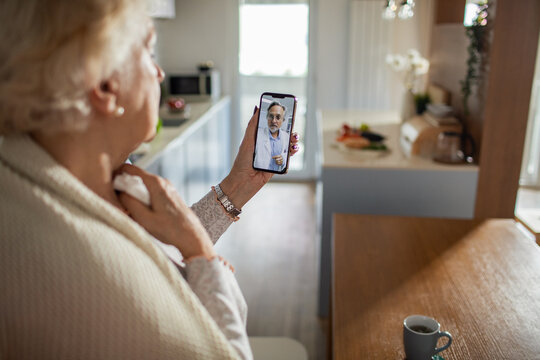 Senior woman having online video call with doctor at home using smartphone