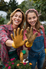 Smiling mother and daughter in garden showing dirty gloves to camera