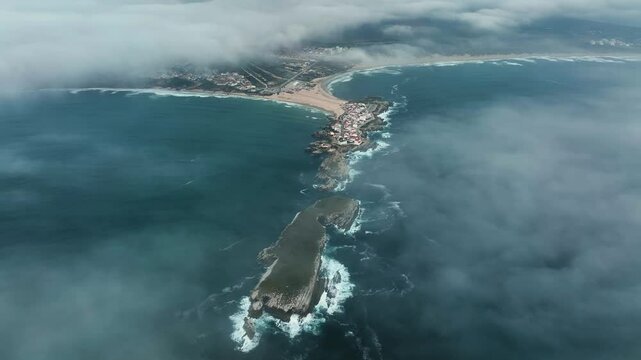 Aerial view of Baleal town and cliffs under cloudy skies across open ocean