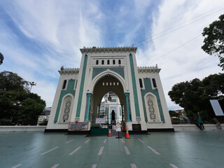 Obraz premium Al-Mashun Grand Mosque in Medan, Indonesia, framed by arch columns, showcasing iconic Islamic architecture under a dramatic cloudy sky