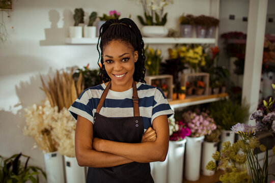 Confident young florist standing in flower shop with arms crossed and smiling at camera