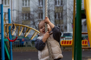 Obraz premium A smiling girl -marsh, rising to a rope on a colorful playground, enjoying classes in the fresh air, developing motor skills and contributing to a feeling of adventure and joy in her childhood.