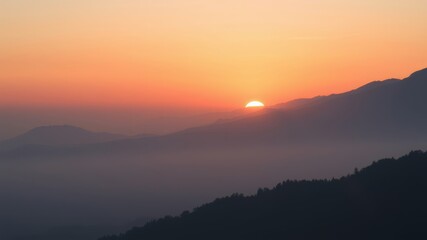 Fototapeta premium A breathtaking sunrise paints the distant mountain range with vibrant orange and pink hues as a soft mist fills the valley below.