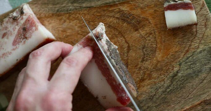 Macro shot of a male hand carefully cutting thin slices of guanciale, ready for a traditional Italian carbonara.