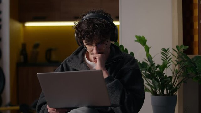 Concentrated Caucasian guy working laptop at home man freelancer programmer chatting website designer in headphones typing online application hipster developer using computer male playing virtual game