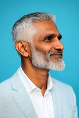 Fototapeta premium Elegant men's high fade haircut - midlife indian man with short hair. Layout art of style for aging men. Blue solid background. A poised man displaying elegance and charm.
