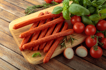 Kabanos sausages with basil and tomatoes on a cutting board.