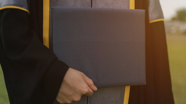 Close-up of a graduate holding a diploma folder in gown, symbolizing academic achievement, success, and new beginnings on a graduation day.