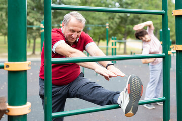 Obraz premium Elderly man doing stretching exercises on a sports bar at an outdoor sports ground