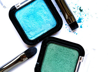 Close-up of shimmering green and turquoise eyeshadows with scattered pigments on a white surface....