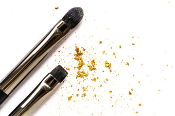 Close-up of scattered gold glitter flakes with a cosmetic brush on a white background. Soft focus...
