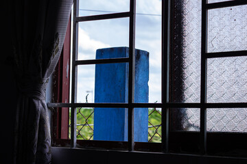 Fototapeta premium View through a window with panes and bars, showing a blue object, greenery, and sky outside, highlighting views or observation.