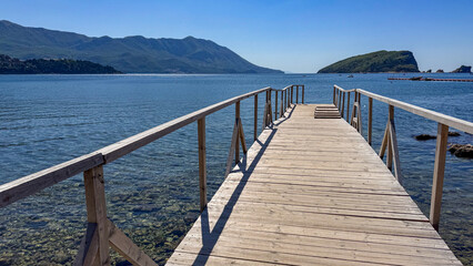 Fototapeta premium Scenic wooden pier extending into calm blue waters with mountains in background