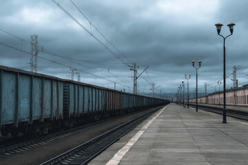 Obraz premium Cargo train parked at deserted railway platform under gray sky, low-saturation wide-angle view