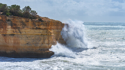 Hohe Welle trifft auf Felsenküste an der Algarve, die Gischt ist höher als der Felsen