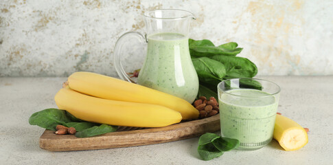 Glass and jug of fresh spinach smoothie with banana and almond nuts on white background