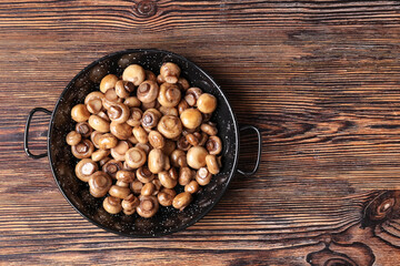 Frying pan with roasted mushrooms on wooden background