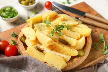 Wooden plate of tasty potato salad with pickled cucumber and tomatoes on white background