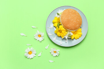 Plate with burger bun and beautiful flowers on green background