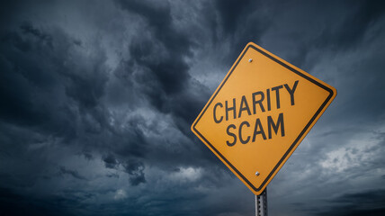 Yellow diamond road sign with text "Charity Scam" against a stormy sky, warning of fraudulent charitable organizations. Symbol of caution and risk.