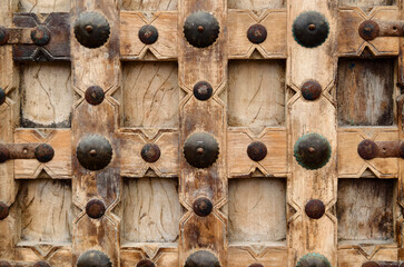 Detailed closeup of an antique wooden door decorated with elegant metal rings mounted on it.