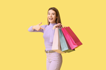 Happy young woman pointing at shopping bags on yellow background