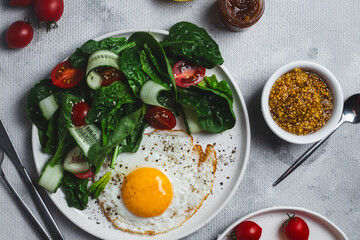 Fried egg with spinach, tomato and cucumber salad in a white plate. Healthy breakfast