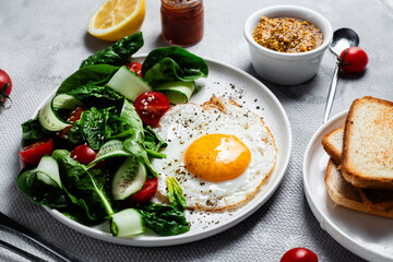 Fried egg with spinach, tomato and cucumber salad in a white plate. Healthy breakfast