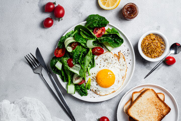 Fried egg with spinach, tomato and cucumber salad in a white plate. Healthy breakfast