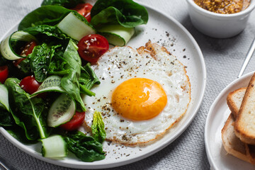 Fried egg with spinach, tomato and cucumber salad in a white plate. Healthy breakfast