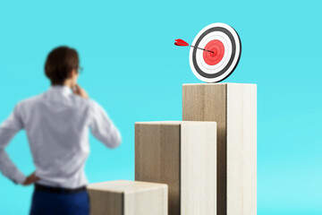 Businessman looking at target with arrow on top of wooden blocks symbolizing success and...
