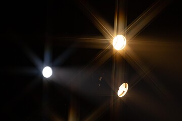 Multiple bright stage lights form vivid starburst patterns against a dark background, creating an...