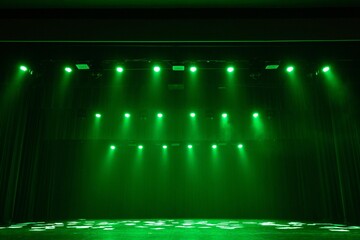 A dimly lit stage bathed in green lighting, with sheets of paper scattered across the floor. Dramatic atmosphere with curtains and stage lights overhead. Copy space included.