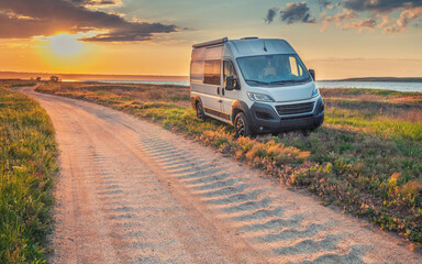 landscape with ground road on coast and white camper van in sunset time