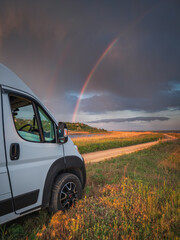 portrait view to head of white van and rainbow in dramatic sky
