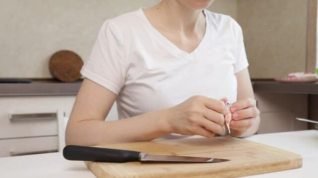 Woman peeling garlic in the kitchen, middle-aged person preparing ingredients, fresh garlic for natural cooking.