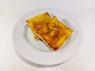 Two slices of golden-brown French toast rest on a stark white plate, their surfaces exhibiting a...