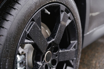 close-up of rain-soaked car tire showcasing intricate tread design and sleek black alloy wheel....